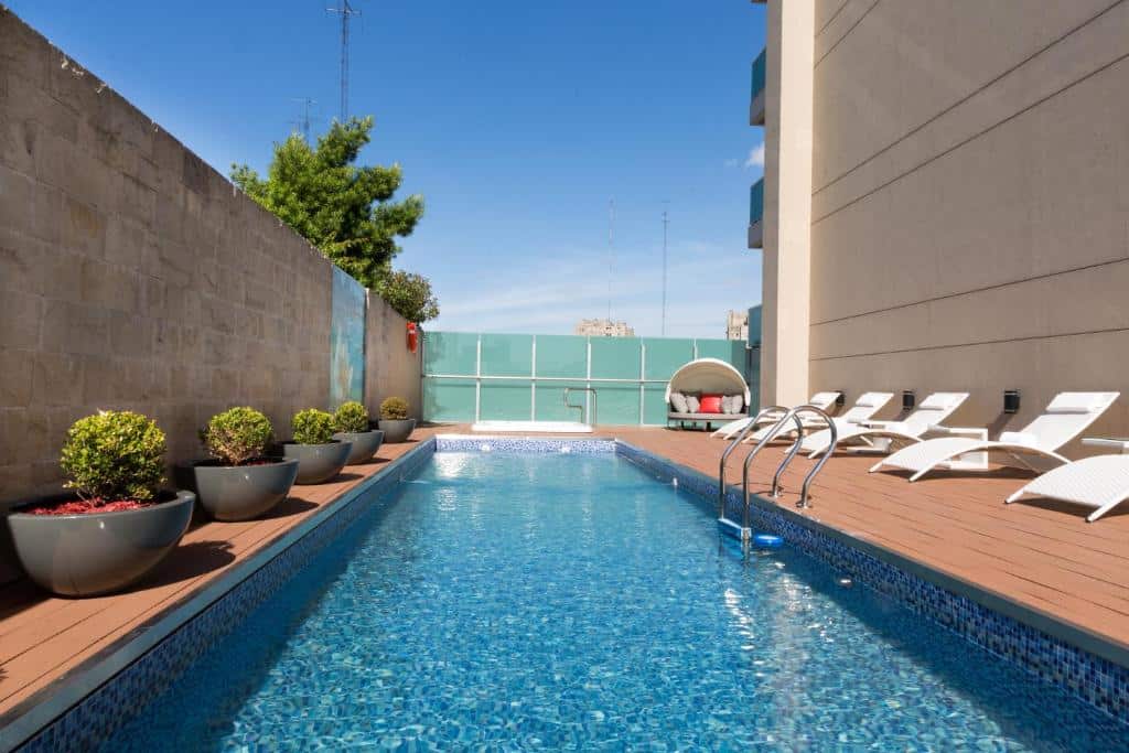 piscina retangular e comprida no terraço do Palladio Hotel Buenos Aires - MGallery, um dos hotéis de luxo em Buenos Aires, de um lado há espreguiçadeiras e, do outro, vaso de plantinhas redondos iguais, o céu está azul
