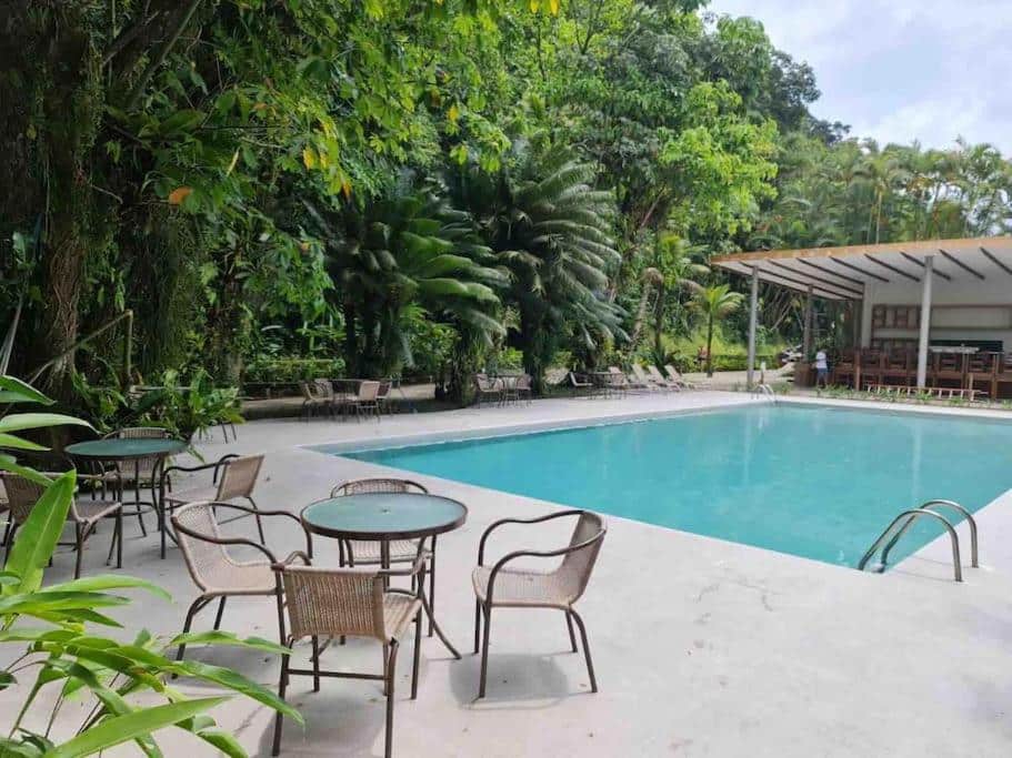 Área de lazer do Delba Costa Smeralda – Barra do Una durante o dia com duas mesas redondas do lado esquerdo da imagem a frente com quatro cadeiras cada e do lado direito a piscina.