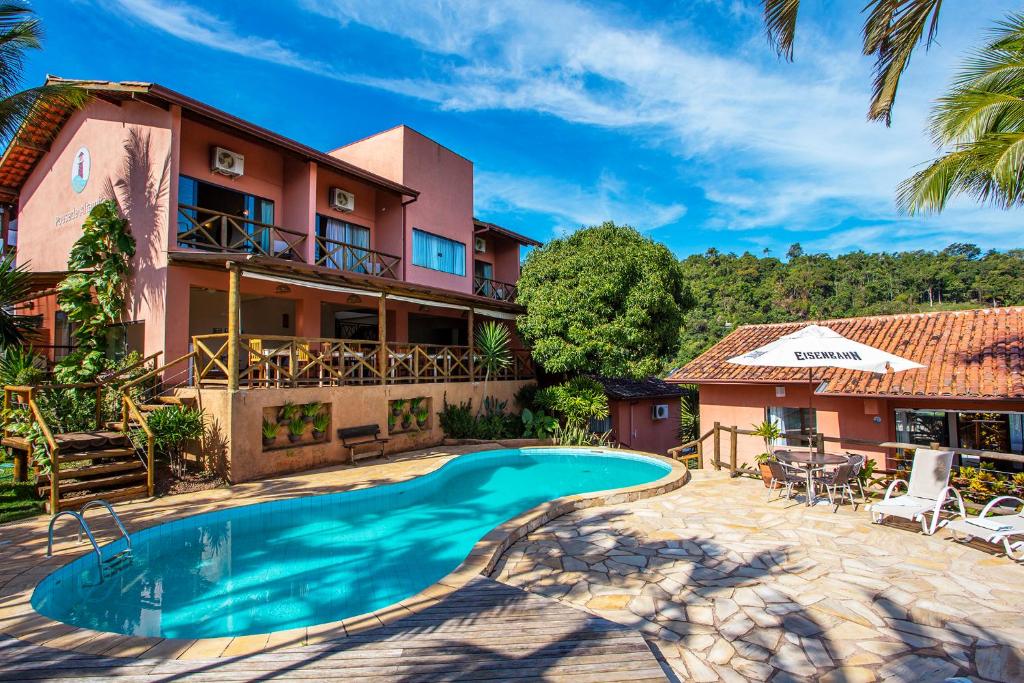 Área externa da Pousada Altamira. Há uma piscina ao centro da imagem, no lado esquerdo há uma pequena escada que vai para uma casa com dois andares, onde ficam alguns quartos. Na direita há algumas espreguiçadeiras, ao fundo uma pequena casa e muitas árvores e plantas.