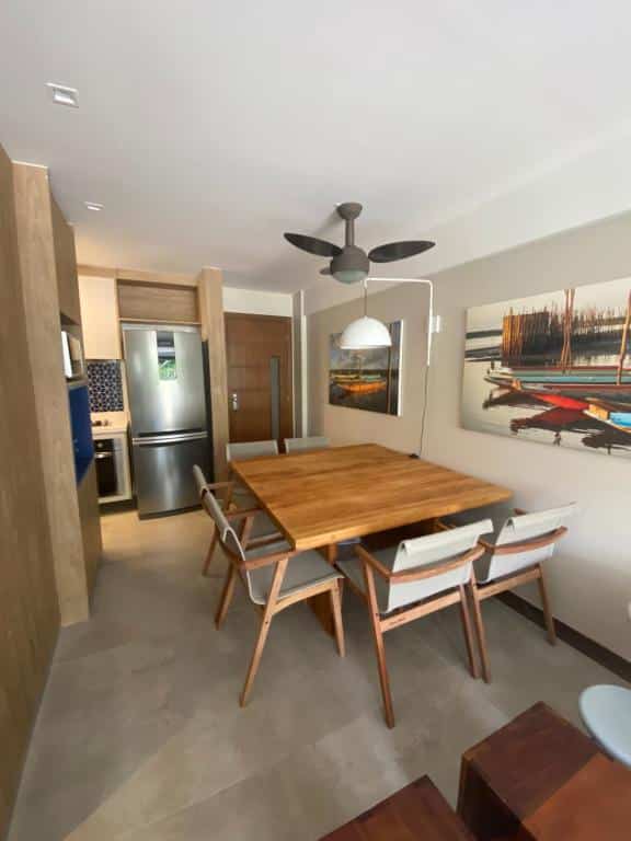 Foto na cozinha da Praia do Forte Condomínio Kauai. É moderno, há uma mesa grande de madeira com seis cadeiras no meio do espaço, e no fundo à esquerda há uma cozinha completa.