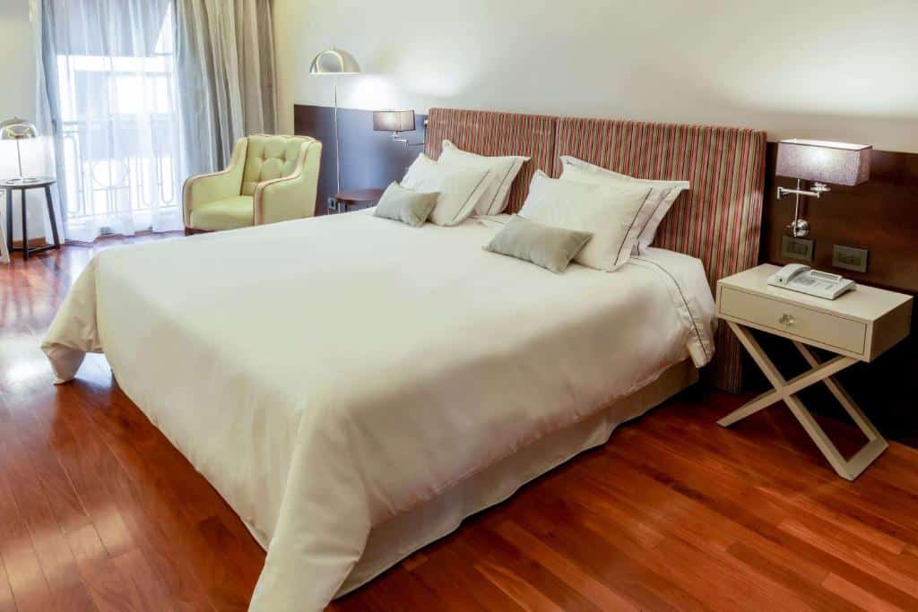 quarto do Esplendor by Wyndham Buenos Aires Tango com cama de casal, mesinha de cabeceira de um lado e luminária em ambos, há uma poltrona em frente a uma janela com cortinas em tons claros