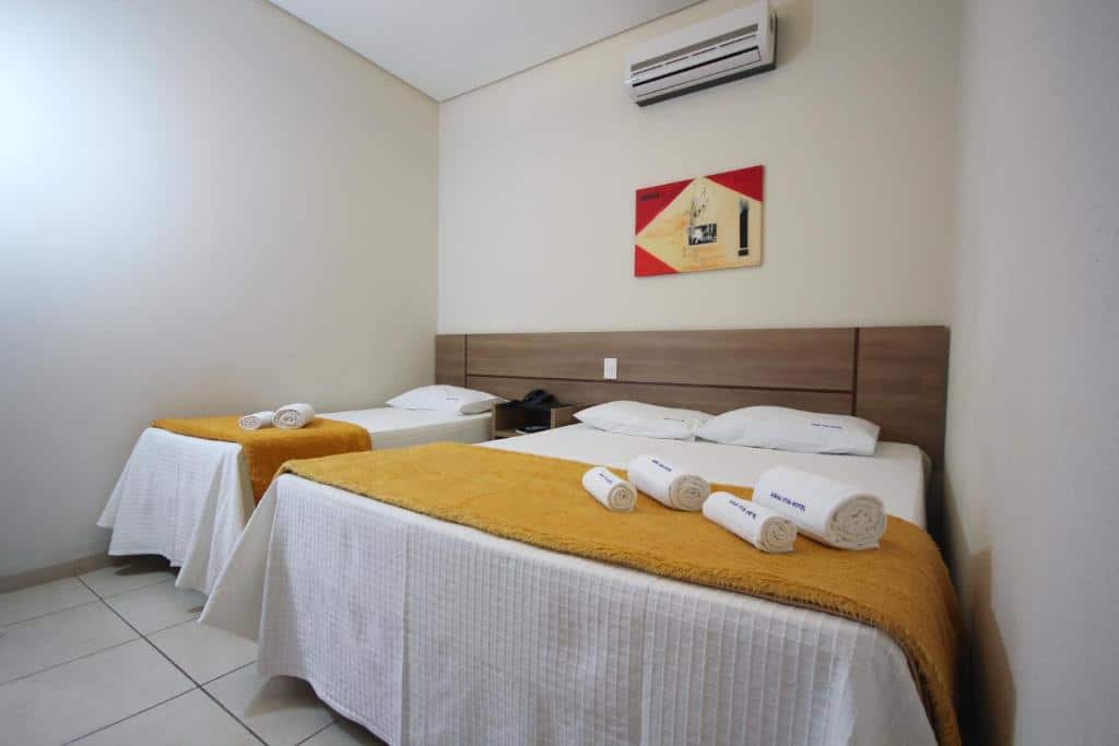 Quarto no Água Viva Hotel com uma cama de casal, uma de solteiro, há um ar-condicionado preso sob as camas, e há também toalhas sob as camas, para representar hotéis em Olímpia