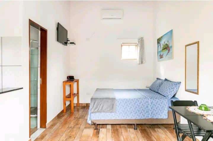 Quarto do Aloha Sertão Flats Ar Condicionado com cama de casal do lado direito da imagem ao fundo e do lado esquerdo da cama uma mesa com cadeira.