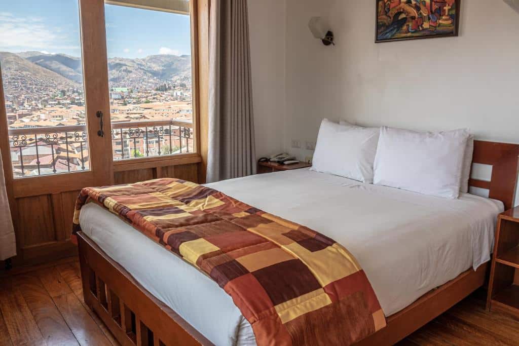 suíte do Amaru Colonial com uma varanda particular no lado esquerdo da imagem, dando vista para toda a cidade de Cusco, além de uma cama de casal no lado de dentro do quarto, parte direita.