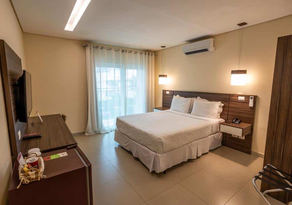 Quarto do Amora Hotel com cama de casal do lado direito da imagem no centro do quarto em frente a cama uma cômoda com TV. Representa airbnb em São Sebastião.