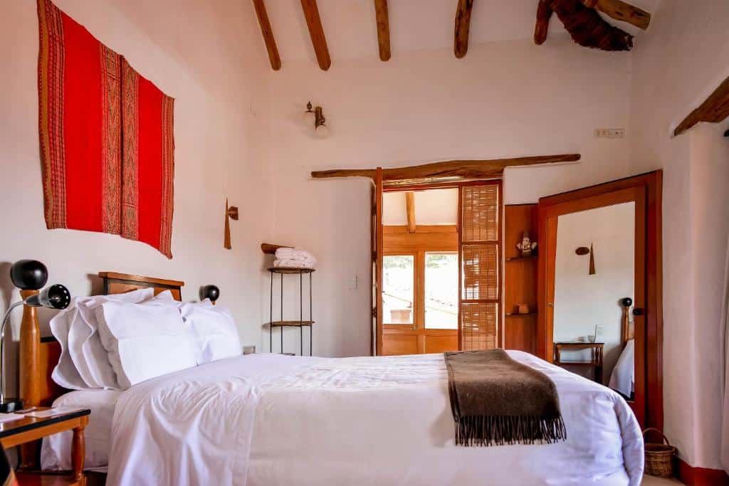 suíte do hotel El Balcón em Cusco com uma cama de casal à esquerda, virado com os pés para a janela. Ao fundo no quatro há uma porta aberta para o corredor do hotel.