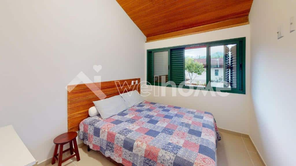 Quarto da Casa em Condomínio na Praia em São Sebastião com cama de casala do lado esquerdo da imagem com um banco do lado esquerdo da cama.