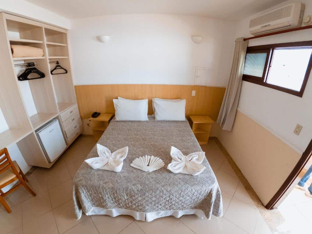 Quarto do Hotel Recanto dos Pássaros com cama de casal no centro do quarto com uma cômoda em cada lado da cama e do lado esquerdo da imagem um guarda-roupa e um frigobar. Representa hotéis em São Sebastião.