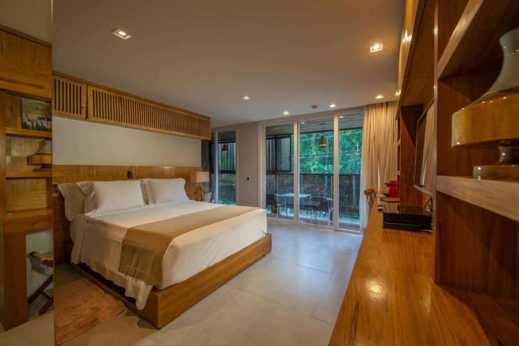 Quarto do Hotel Spa Nau Royal com cama de casal do lado esquerdo da imagem no centro do quarto com uma luminária do lado esquerdo da cama e em frente a cama uma cômoda com TV em cima. Representa airbnb em São Sebastião.