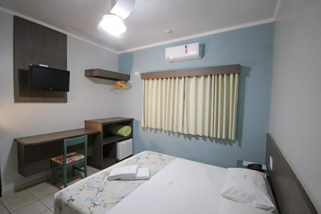Quarto do Hotel Villa Rebellato  com uma cama de casal, uma janela com cortinas, de frente para a cama há uma televisão, uma mesa de escritório, um pequeno armário com toalhas e um cabideiro