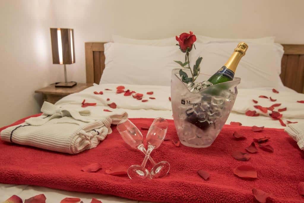 Quarto do Ilha de Toque Toque Eco Boutique Hotel & Spa com cama de casal no centro da imagem com pétalas de rosas em cima e um balde de champanhe com duas taças. Representa hotéis em São Sebastião.