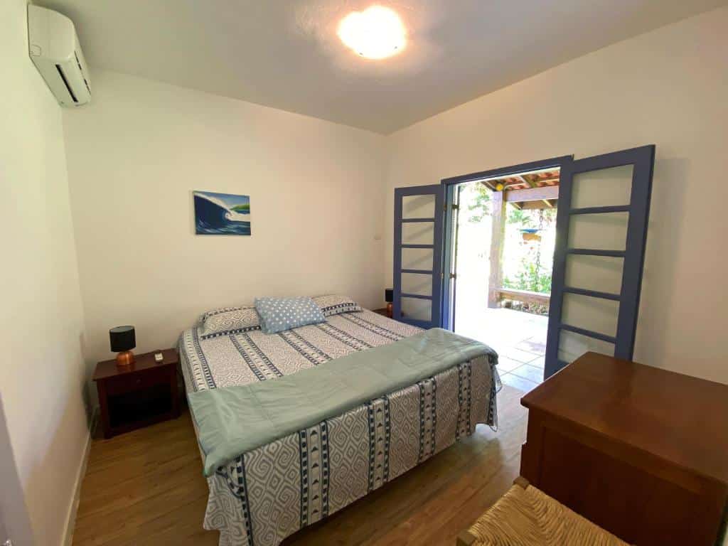 Quarto do Juréia Dreams com cama de casal do lado esquerdo da imagem no centro do quarto e em cada lado da cama uma cômoda com luminária. Representa airbnb na praia do Engenho.