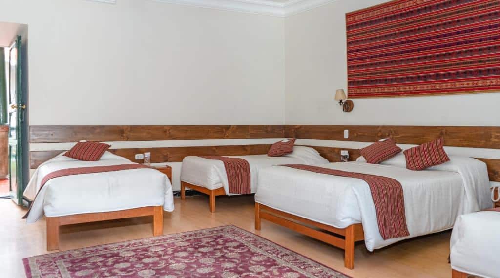 quarto familiar da La Casona Real Cusco com quatro camas e um tapete rosado disposto no chão, entre as camas.