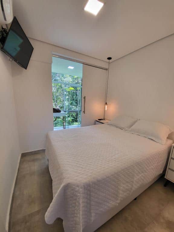 Quarto do Maresias Beach Housing com cama de casal do lado direito da imagem em cada lado da cama uma cômoda e em frente a cama na parede uma TV. Representa airbnb em São Sebastião.