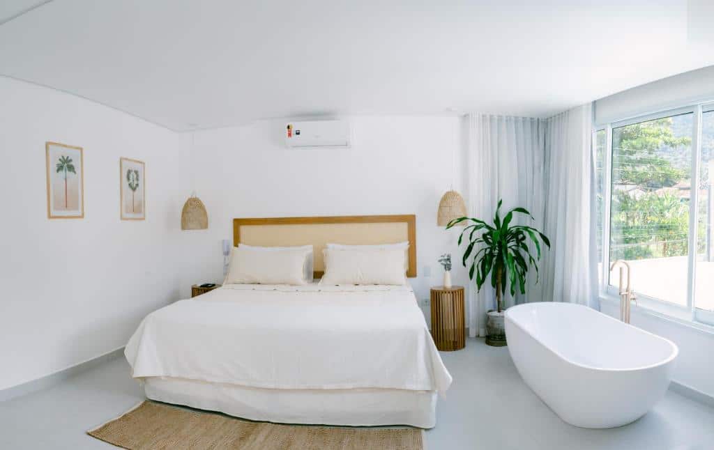 Quarto do Olisa Hotel Boutique com cama de casal no centro do quarto e em cada lado da cama uma cômoda e do lado esquerdo da cama uma banheira de hidromassagem. 