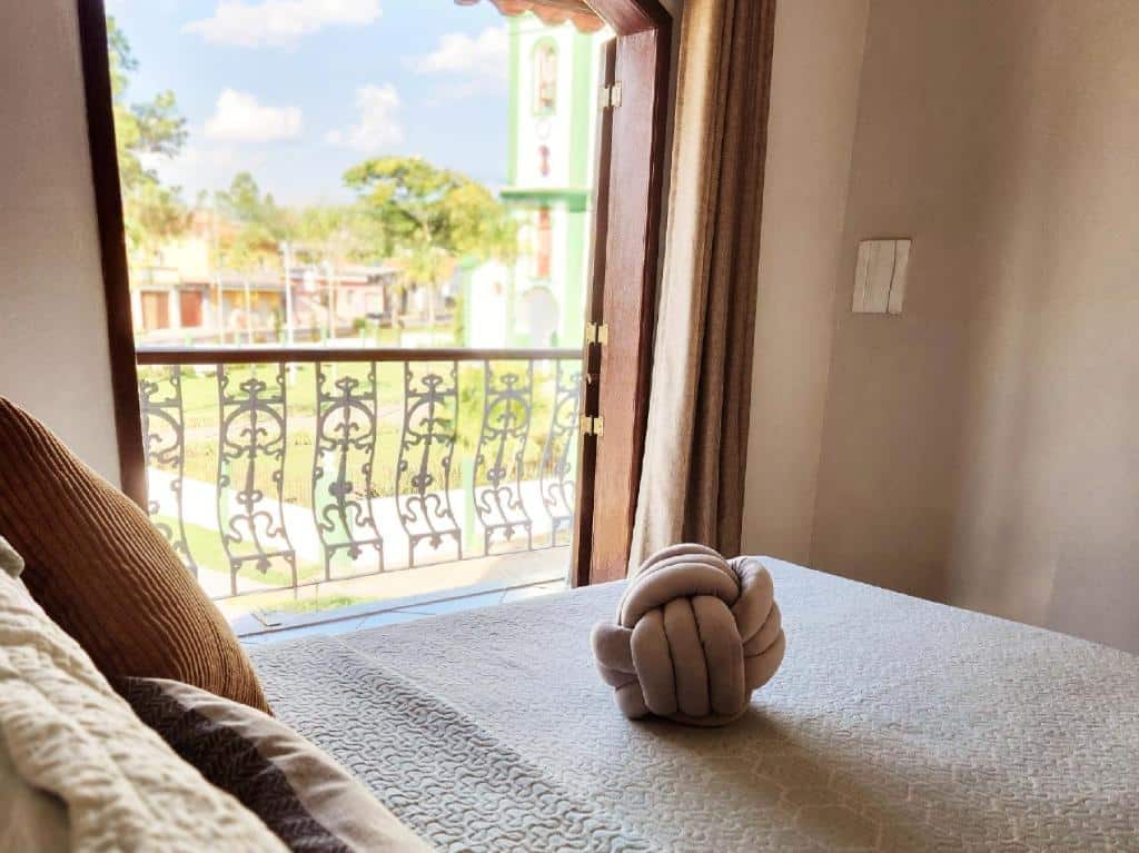 Quarto do PousaDinháChica Hospedagem com cama de casal do lado esquerdo da imagem e do lado esquerdo da cama uma porta com acesso a varanda.