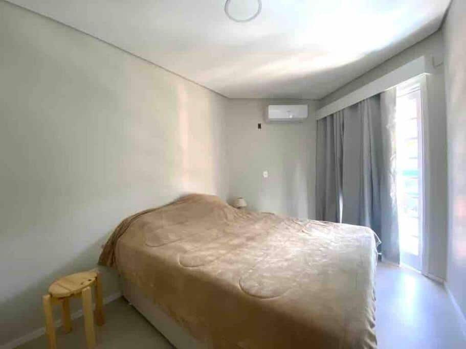 Quarto da Praia do Engenho – Apart Lindo e Novíssimo 30m da praia com cama de casal do lado esquerdo da imagem no centro do ambiente em cada lado uma cômoda e do lado direito da cama na cômoda uma luminária. Representa airbnb na praia do Engenho.