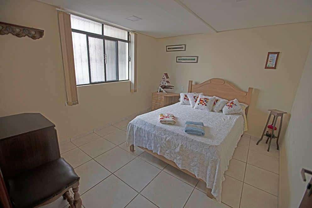 Quarto do Recanto São Francisco com cama de casal do a frente no centro do ambiente com uma cômoda do lado direito da cama e um móvel do lado esquerdo.