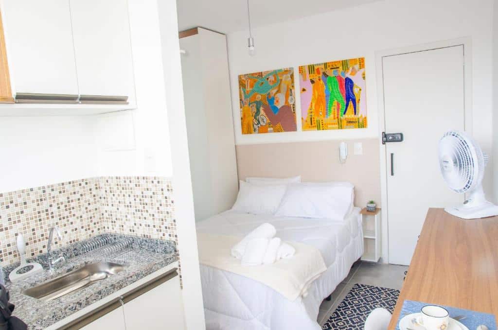 Imagem do Studio 900m do centro com uma pia do lado esquerdo da imagem ao fundo uma cama de casal e do lado esquerdo da imagem uma cômoda com ventilador. Representa airbnb em São João del Rei.
