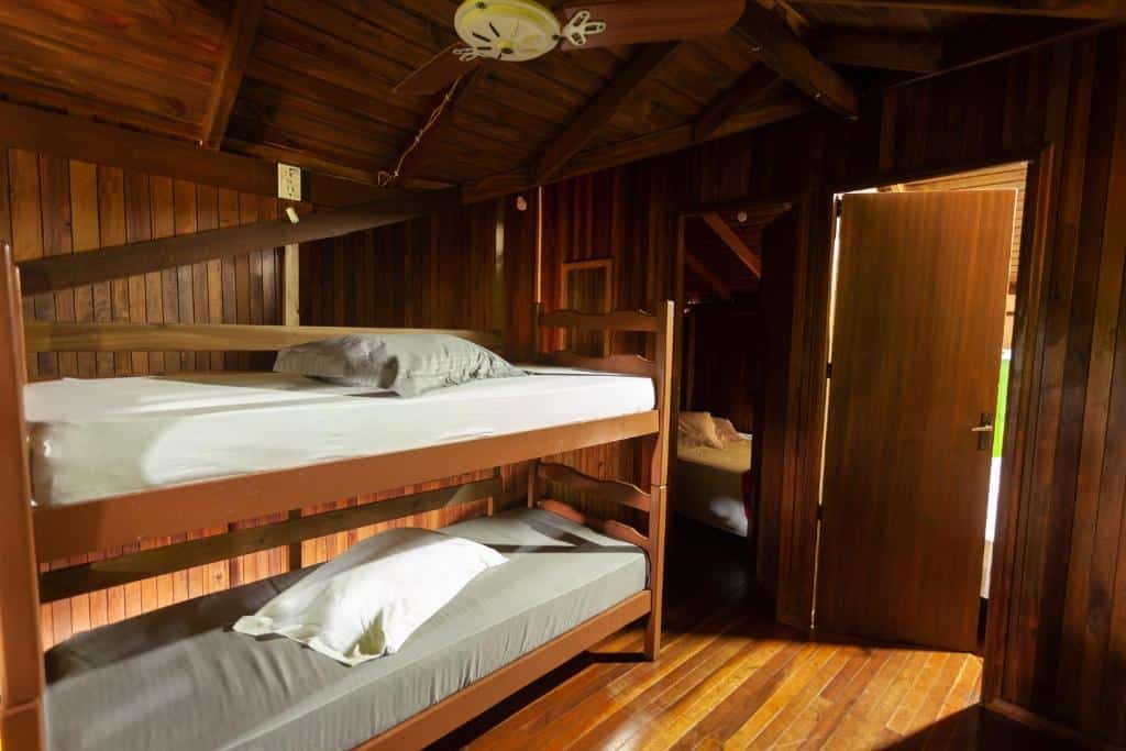 Quarto do Recanto do Sossego, airbnb em Garopaba. Uma beliche está encostada na parede ao lado esquerdo e tem um espelho logo em frente. Ao lado do espelho fica a porta para fora. O chalé é todo de madeira.