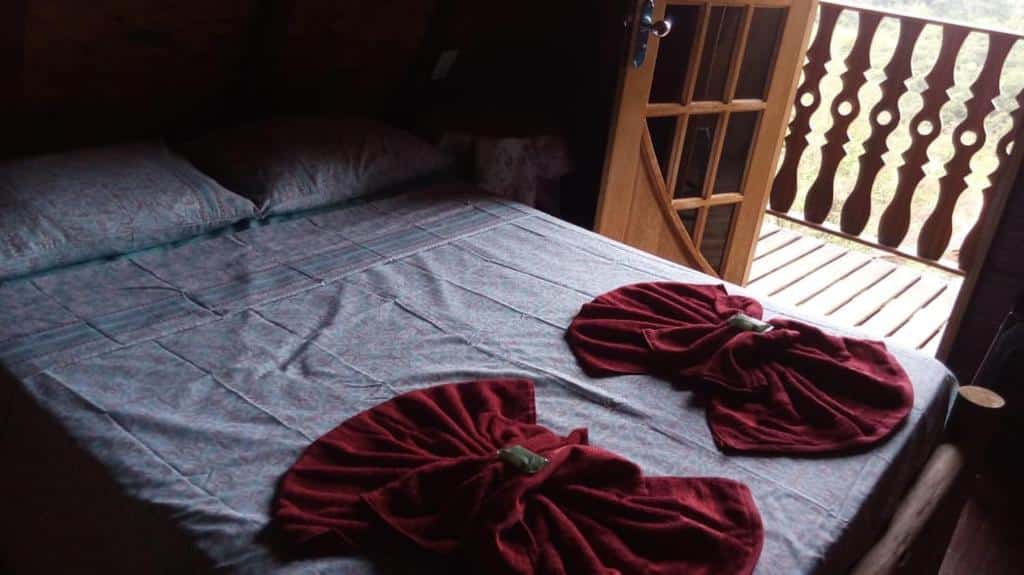 Imagem do quarto em Recanto Mauá - Chalé Amor Perfeito, que está ilustrando o post sobre airbnb em Visconde de Mauá. A cama é de casal e do seu lado direito há uma porta com varanda e vista.