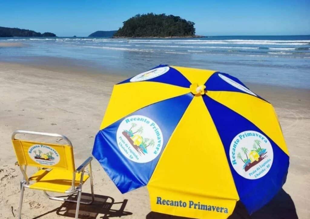 Cadeira de praia e guarda-sol do  Recanto Primavera Ubatuba. Eles estão na areia da praia, de frente para o mar.