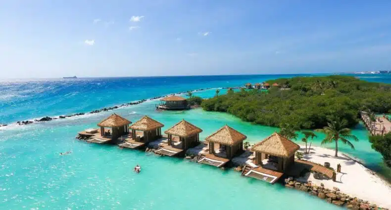 Cabanas do Renaissance Wind Creek Aruba Resort na ilha privativa. Ela estão em uma curta faixa de areia no meio do mar. Ao fundo é possível ver diversas árvores, para representar resorts em Aruba