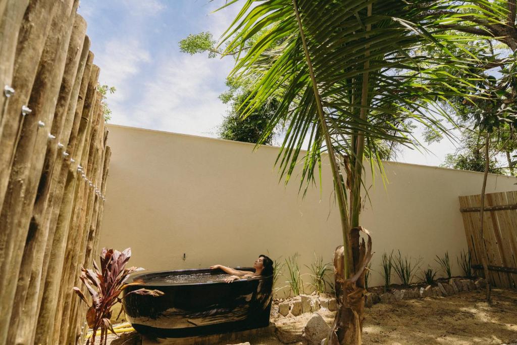 Área externa do quarto da pousada Reserva Ilhabela. Há uma banheira a esquerda, cercada por um muro de concreto ao fundo e uma cerca alta de madeira em volta de toda a área do quintal, que tem chão de terra e algumas plantas também.