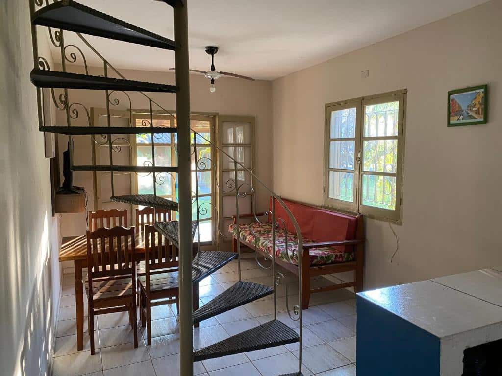 Sala do Residencial As Corujas. Ao fundo é possível ver um sofá de frente para uma tv e uma mesa de quatro lugares. No meio há uma escada em formato caracol. Ele faz parte dos airbnb em Boiçucanga.