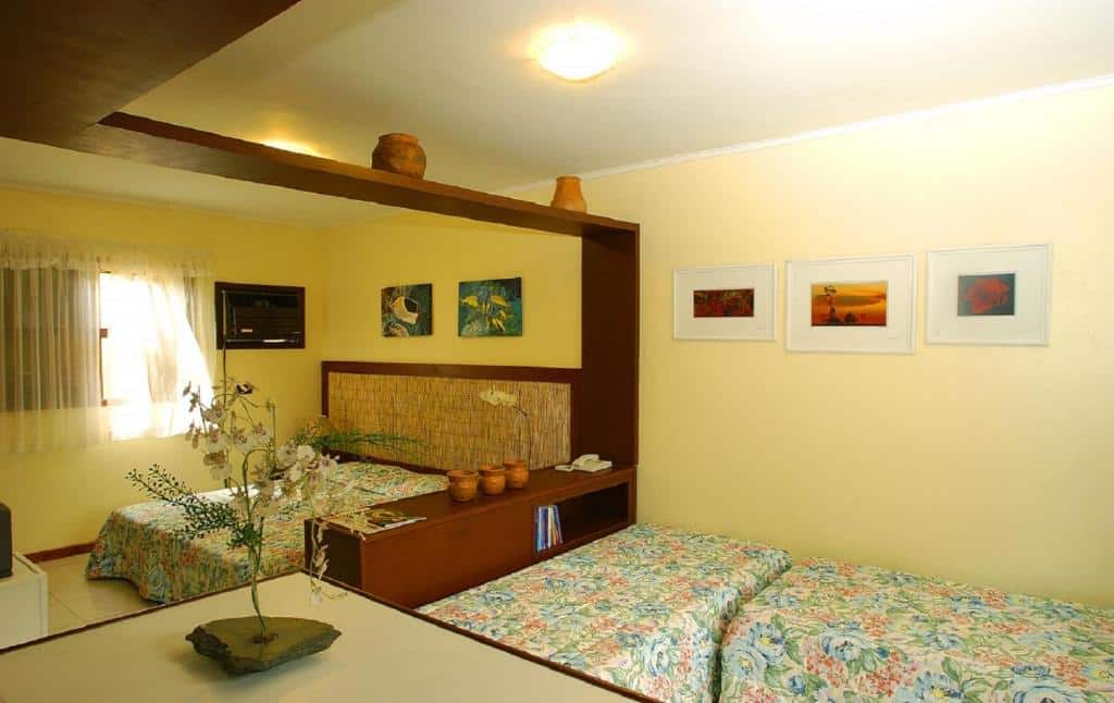 Quarto do Residencial Vilamar, um dos airbnb em Ilhabela. O ambiente é dividido em dois: ao lado direito estão duas camas de solteiro, enquanto ao lado esquerdo está a cama de casal e uma TV. Um móvel de madeira fica entre os dois cômodos.