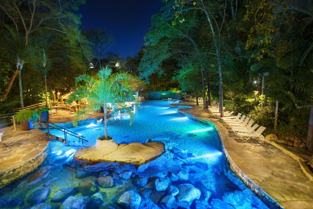 Piscina do Hotel Turismo. Uma piscina de água termal natural com pedras, de cada lado cadeiras de tomar sol e escadas e árvores.
