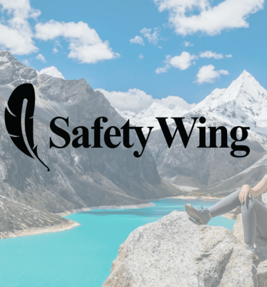 Uma paisagem com um lago de azul muito azul cortando diversas montanhas, em uma dessas montanhas há uma mulher sentada olhando a paisagem, para representar SafetyWing Seguro Viagem