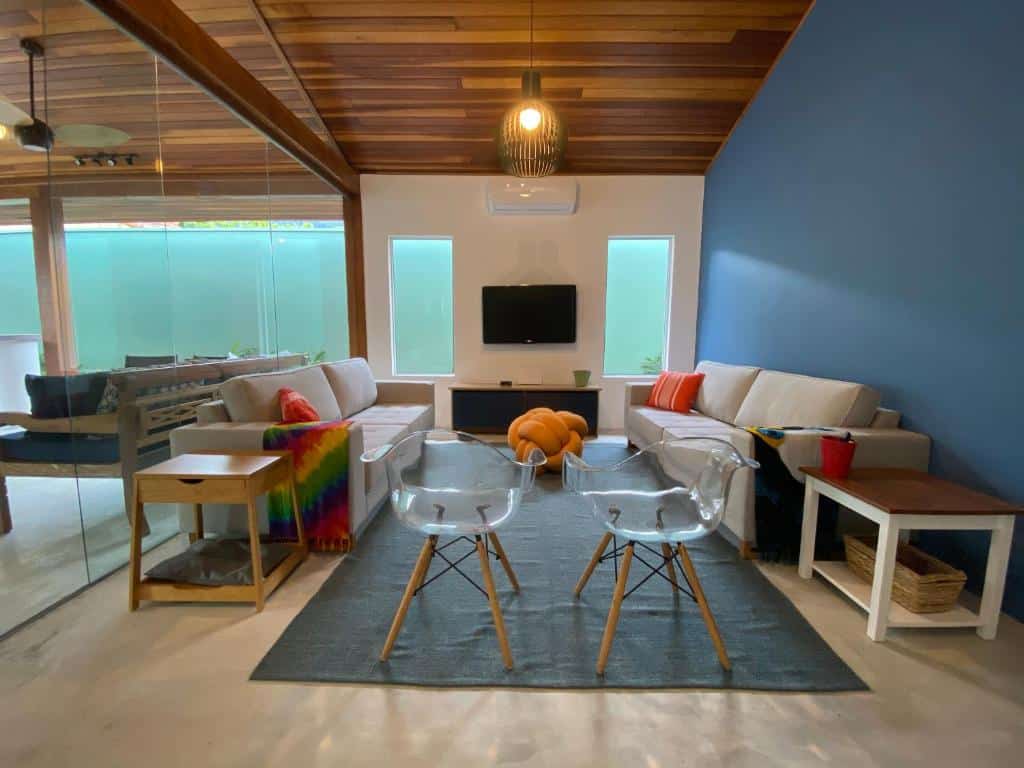 Sala de estar da Casa Amendoeiras – spa aquecido e wifi com duas cadeiras a frente e do lado direito e esquerdo uma mesa com sofá em cada lado no centro do ambiente um cômoda com TV presa na parede.