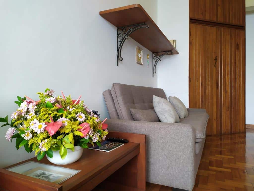 Imagem de uma mesa com flores do lado esquerdo da imagem e um sofá-cama no Flat aconchegante no Centro Histórico.