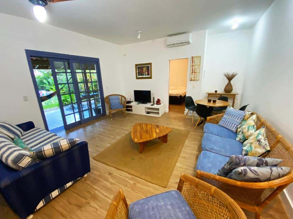 Sala de estar Juréia Dreams com sofá do lado direito da imagem do lado esquerdo um sofá de dois lugares e no centro uma mesa de madeira.