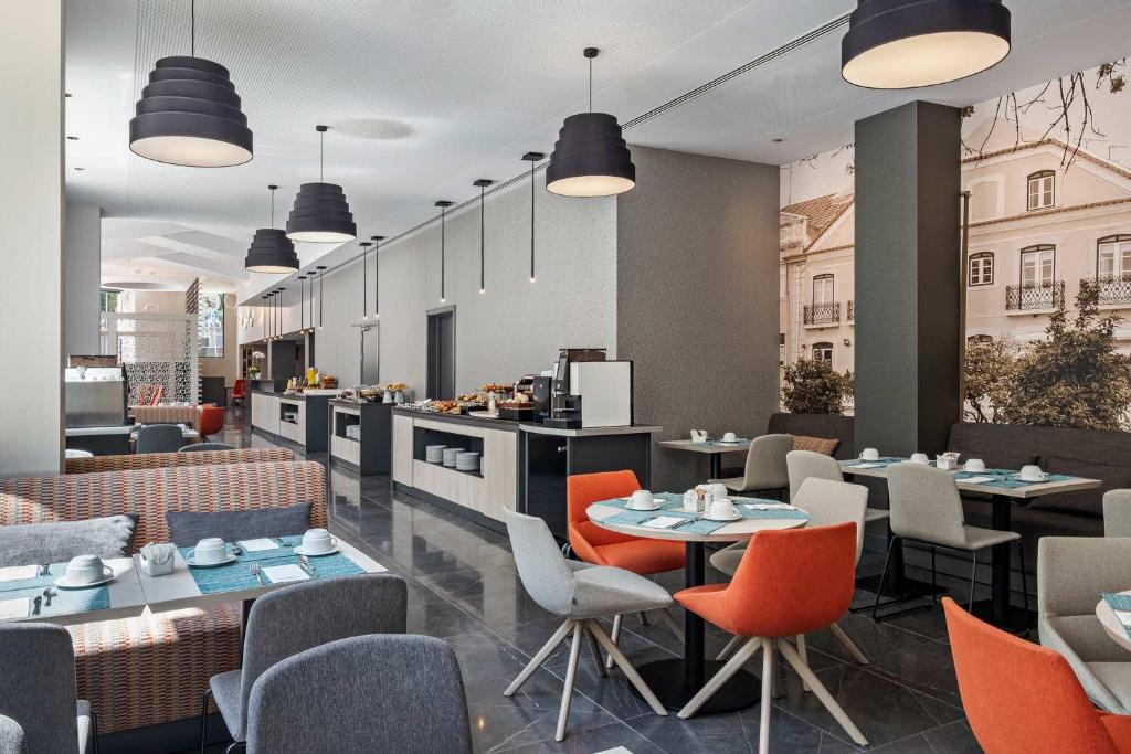 Área de refeições do EXE Liberdade com balcões extensos com itens de café da manhã, há mesas redondas, cadeiras estofadas e sofázinhos para sentar-se no local