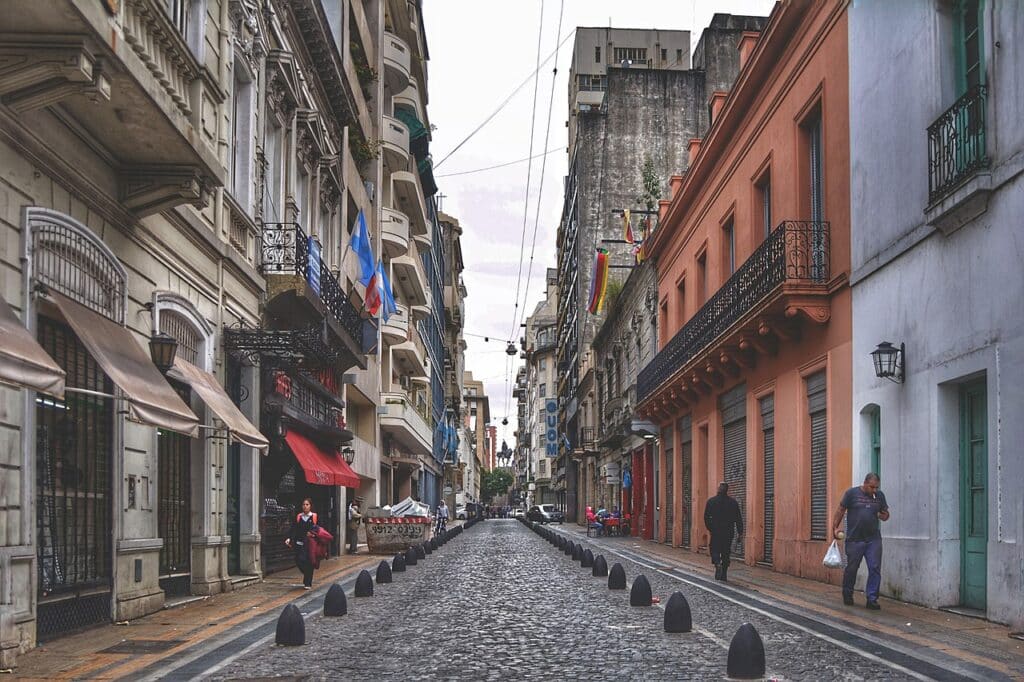 Ruas de paralelepípedo em San Telmo ladeadas por prédios. Algumas pessoas caminham nas laterais.