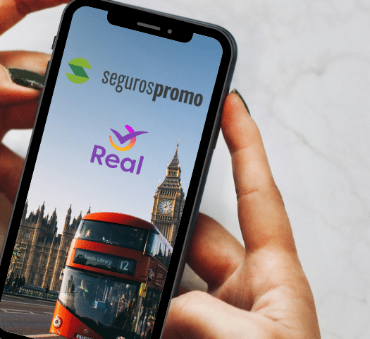 Duas mãos negras segurando um celular, enel há uma imagem de Londres com os logos das duas empresas em cima, para representar Seguros Promo ou Real Seguro Viagem