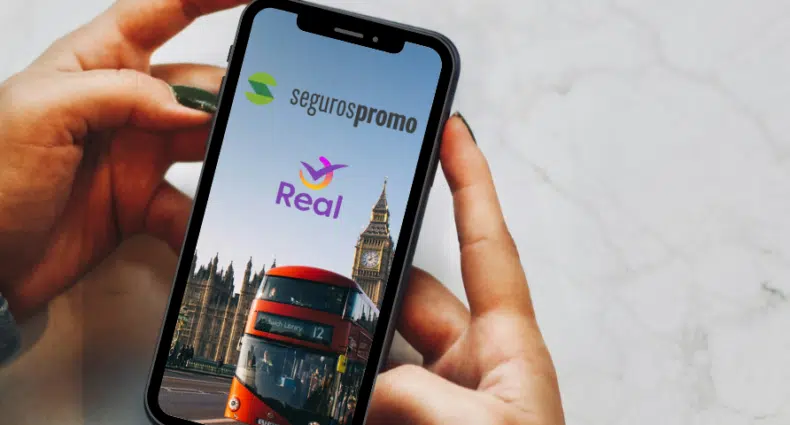 Duas mãos negras segurando um celular, enel há uma imagem de Londres com os logos das duas empresas em cima, para representar Seguros Promo ou Real Seguro Viagem