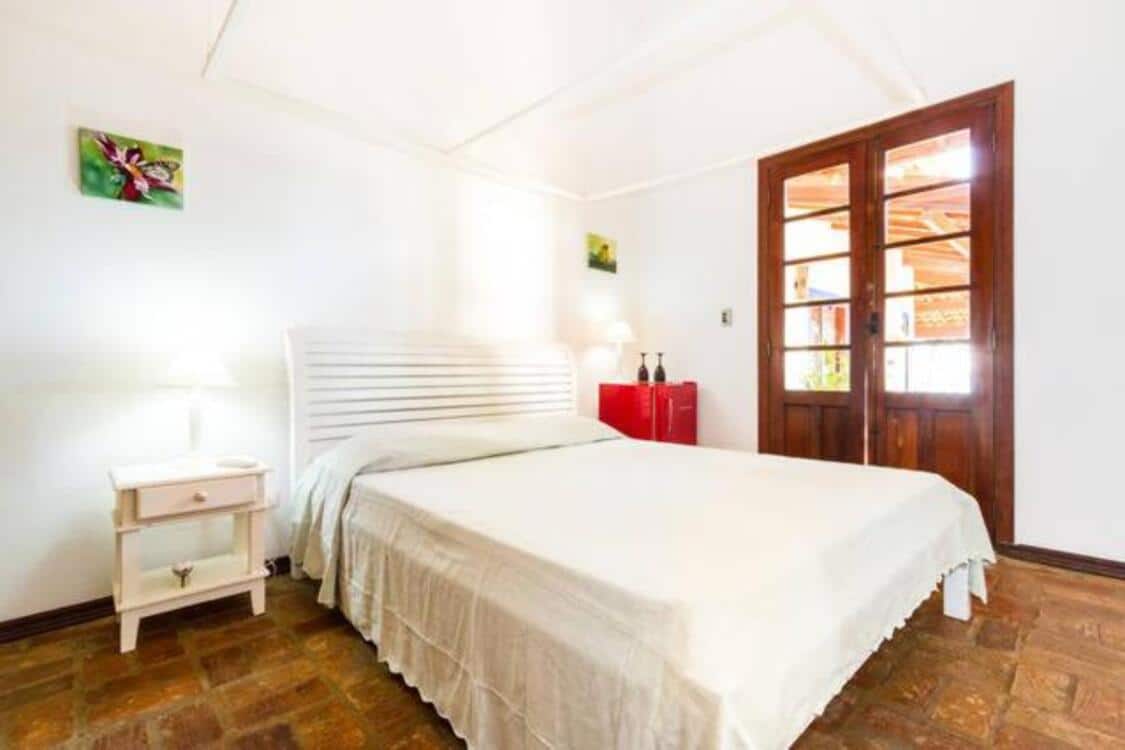 Quarto das Suites e Bungalow Sol-Lua, um dos airbnb em Ilhabela. Uma cama de casal tem mesinhasa de cabeceira com abajures dos dois lados. Na lateral direita fica a porta.