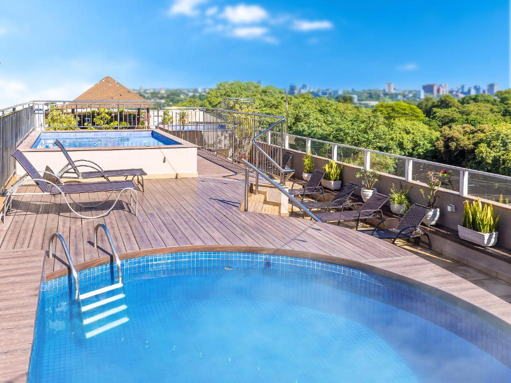 Parte do Tarobá Hotel que mostra duas piscinas ao ar livre em cima de um deck de madeira no último andar do prédio. As piscinas tem vista para as árvores e construções da cidade. Imagem ilustrando post Hotéis em Foz do Iguaçu.