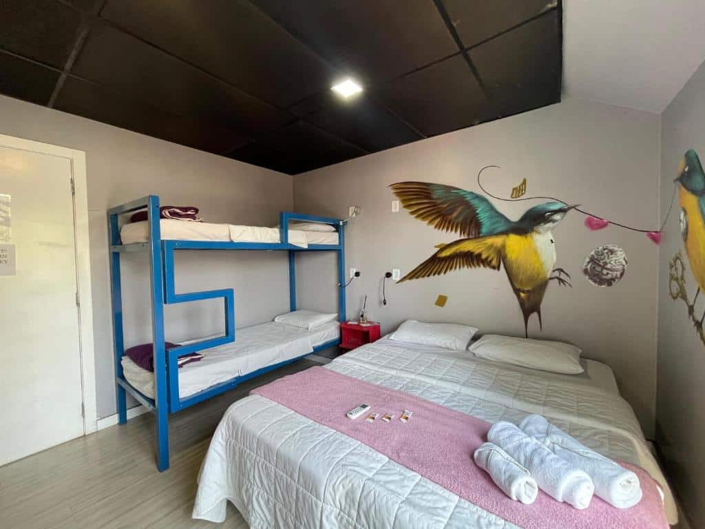 Foto do quarto do Tetris Container Hostel, ilustrando o post sobre Onde ficar em Foz do Iguaçu. Há uma cama box de casal na direita, e ao seu lado, na esquerda, há uma beliche. A parede atrás delas há um desenho de beija-flor.