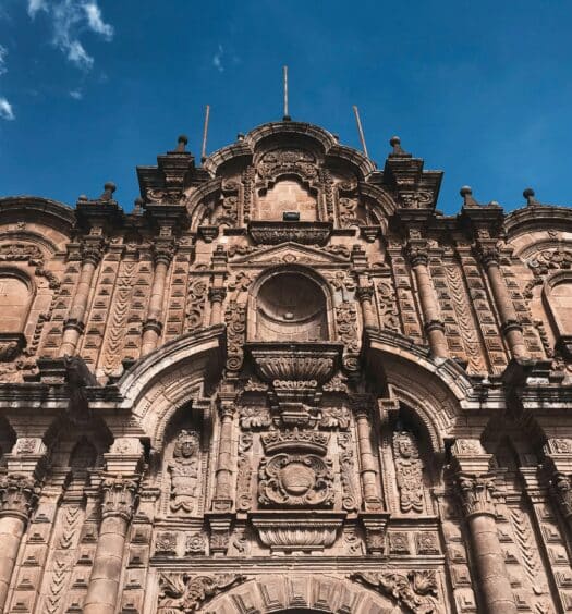 Vista frontal da Catedral Basílica da Virgem da Assunção em Cusco mostrando a entrada de pedra da igreja com uma bela arquitetura.