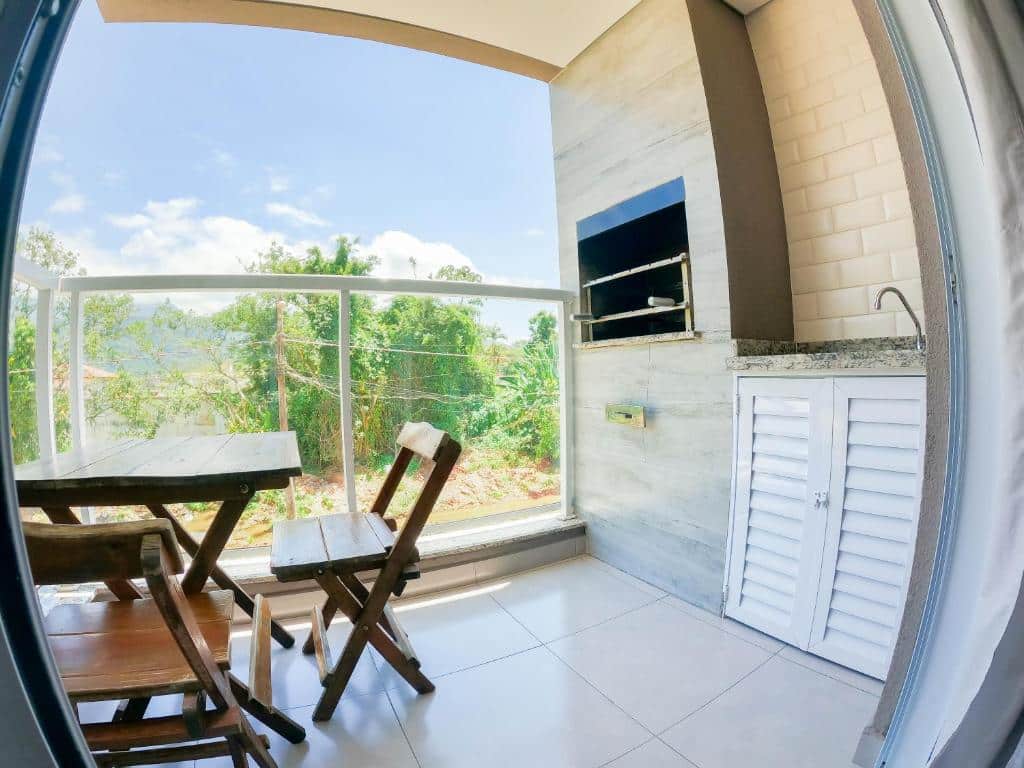 Varanda do Ubatuba Prime House ap106 que mostra do lado esquerdo uma mesa de madeira com duas cadeiras e do lado esquerdo uma pia para lavar louças com um armário embaixo e do lado uma churrasqueira. Imagem ilustrando post Airbnb em Maranduba.