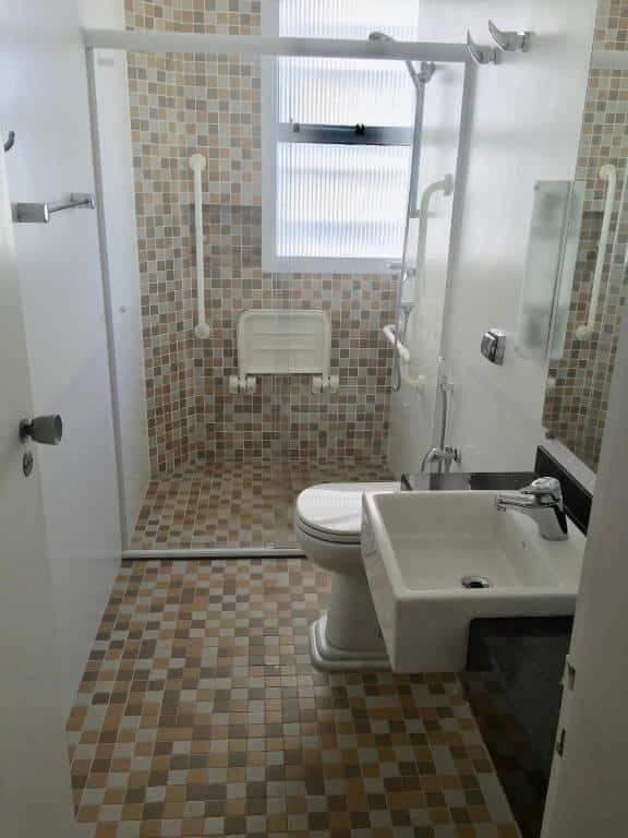 Banheiro do Vista Maravilhosa Pintangueiras com pia rebaixada, vaso sanitário elevado e box com barras de apoio e cadeira de banho.