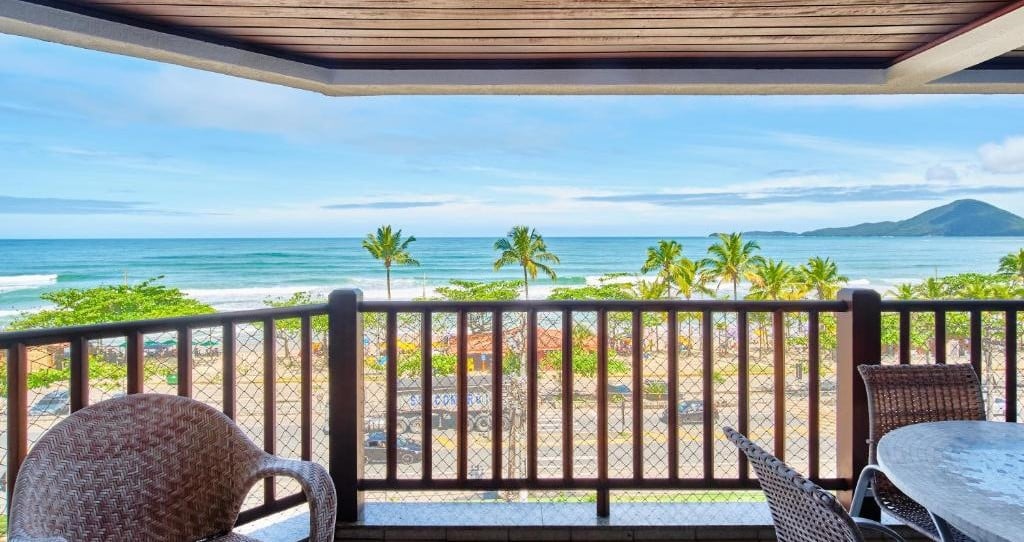 Vista da varanda do Vista Panorâmica do Mar. Uma sacada na frente com uma incrível vista de palmeiras e o mar. Foto para ilustrar post sobre airbnb na Praia Grande de Ubatuba.