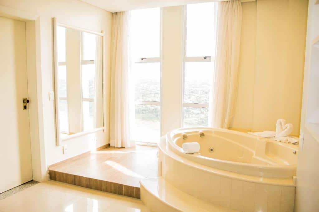 Foto do Wyndham Golden Foz Suítes, mostrando outro ângulo do quarto com uma banheira de hidromassagem e uma janela do lado.