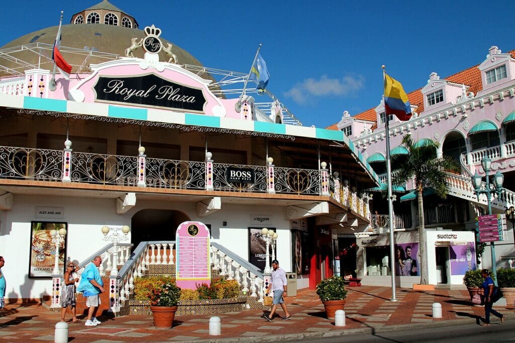 vista da rua com pessoas passando e a entrada do Royal Plaza, em Oranjestad, um lugar onde fazer compras em Aruba ao estilo colonial holandês, parecendo uma tenda com cores azuis pasteis