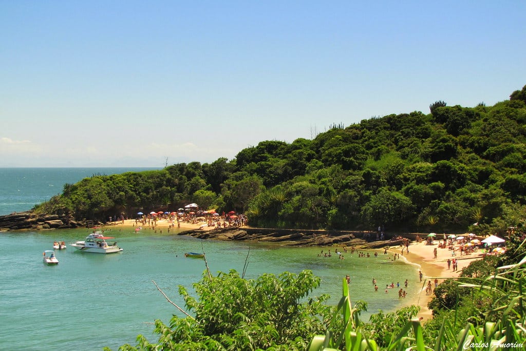 Vista da Praias Azeda e Azedinha. Um pouco de árvores na frente, atrás a vista das duas praias com bastante pessoas e duas lanchas no mar.