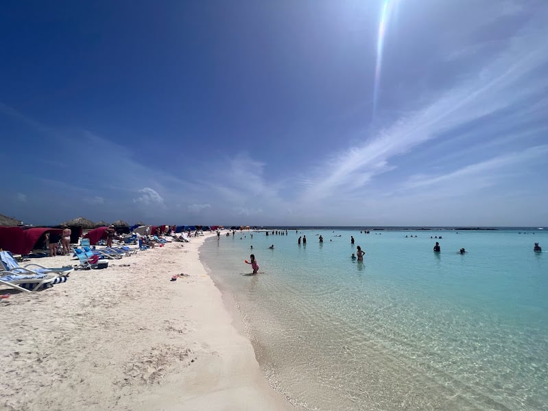 Imagem da praia de Baby Beach durante o dia com faixa de areia do lado esquerdo da imagem e do lado direito o mar com pessoas dentro. Representa Aruba.